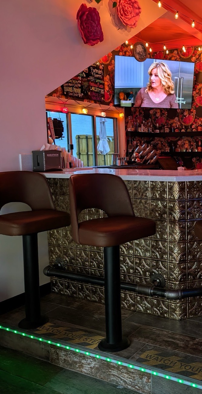 The inside bar with pressed tin panels, leather stools, framed portrait wallpaper and warm string lighting