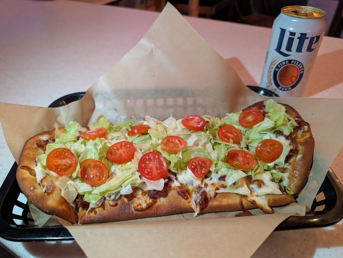A BLT flatbread pizza topped with lettuce and tomato, next to a cold beer