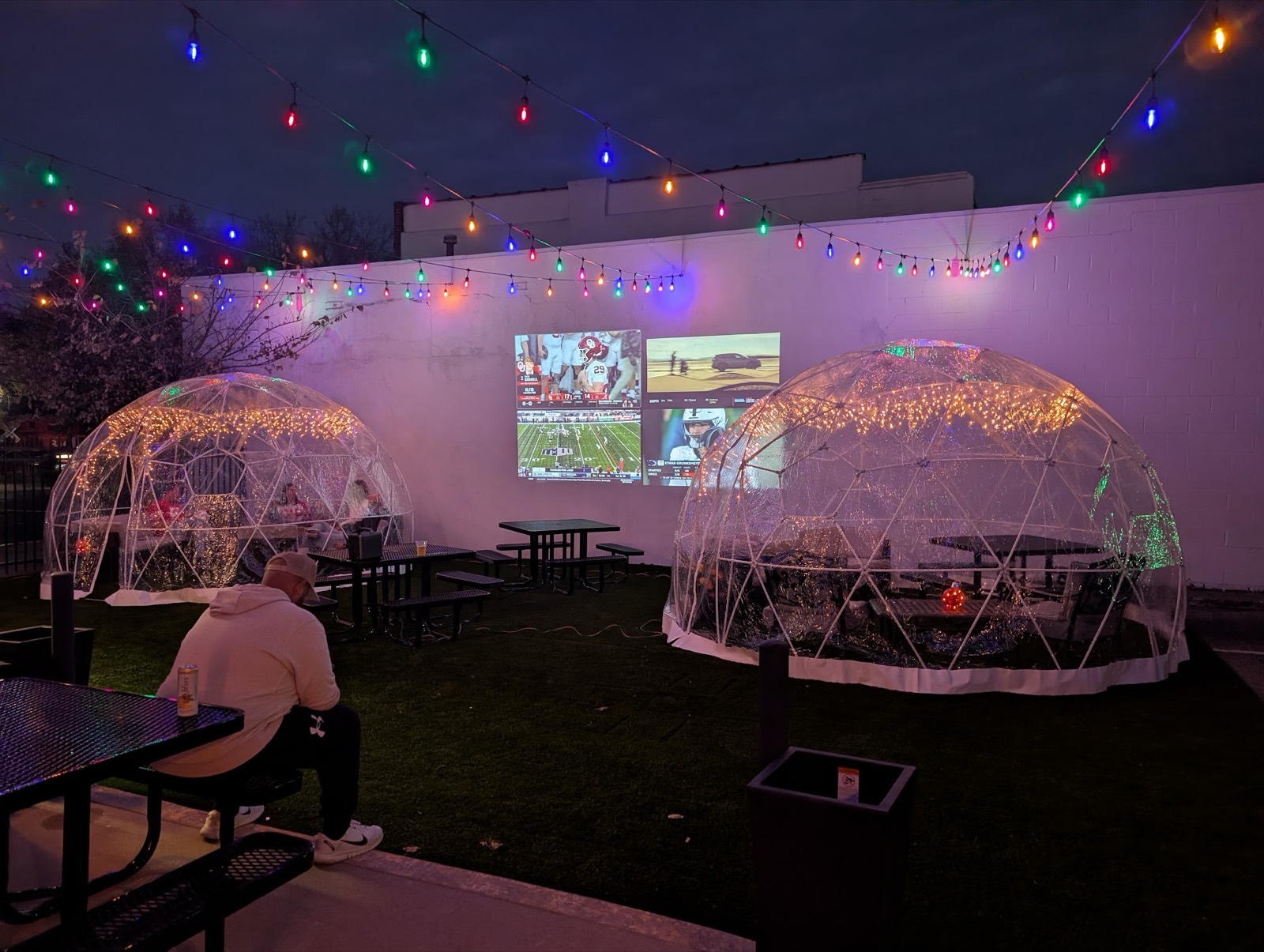 Two lit igloo domes in the courtyard with string lights overhead and televisions mounted on the wall