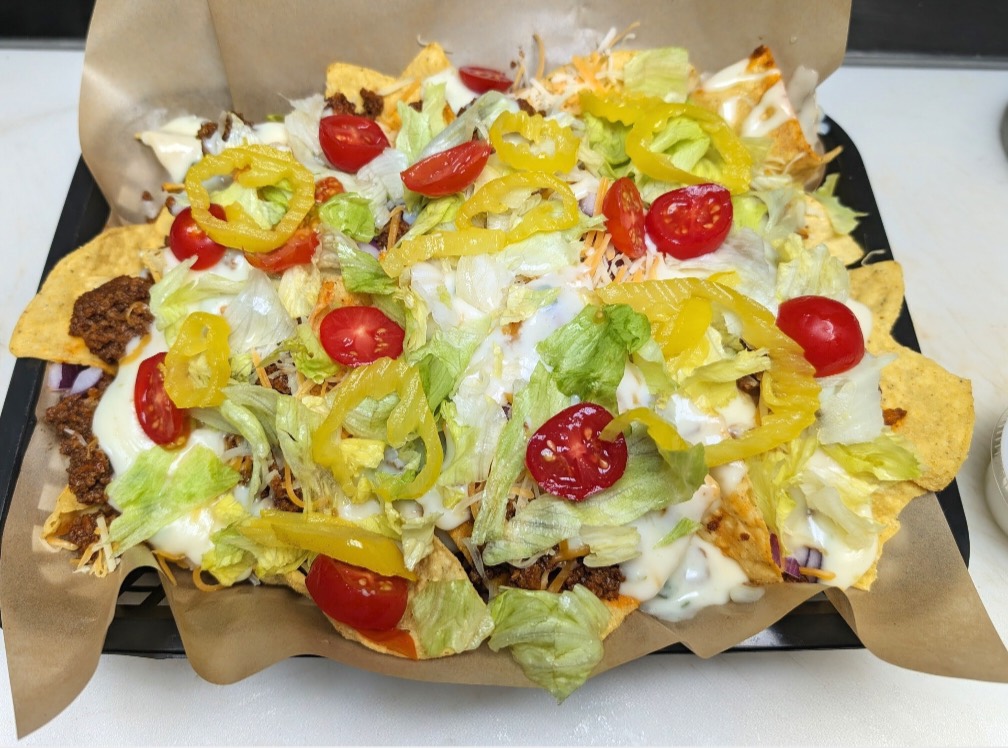 A tray of loaded nachos with taco beef, queso, lettuce, tomatoes and banana peppers