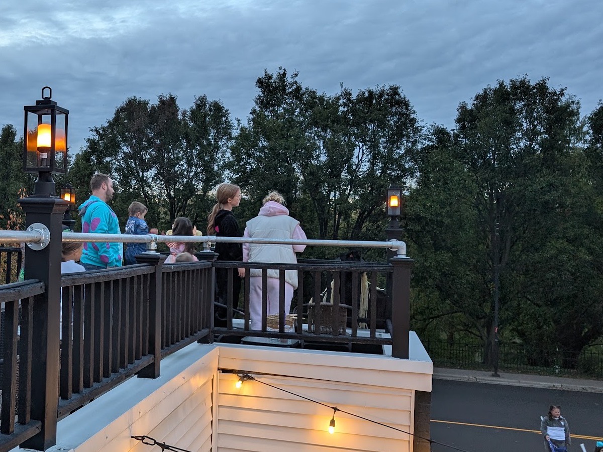 Families with young children at the rooftop railing at dusk, lanterns lit along the deck