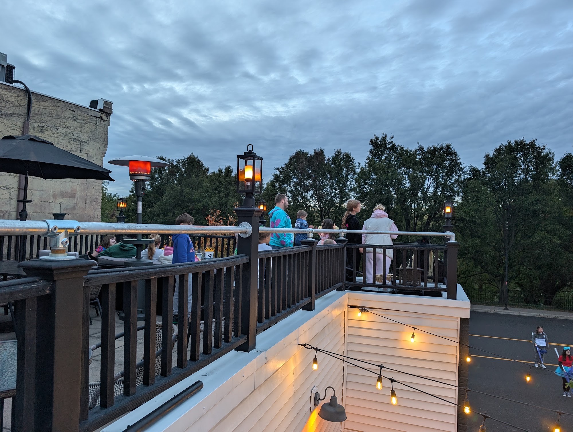 The open rooftop deck at dusk, strung with lights, looking out over the treeline of Yoctangee Park