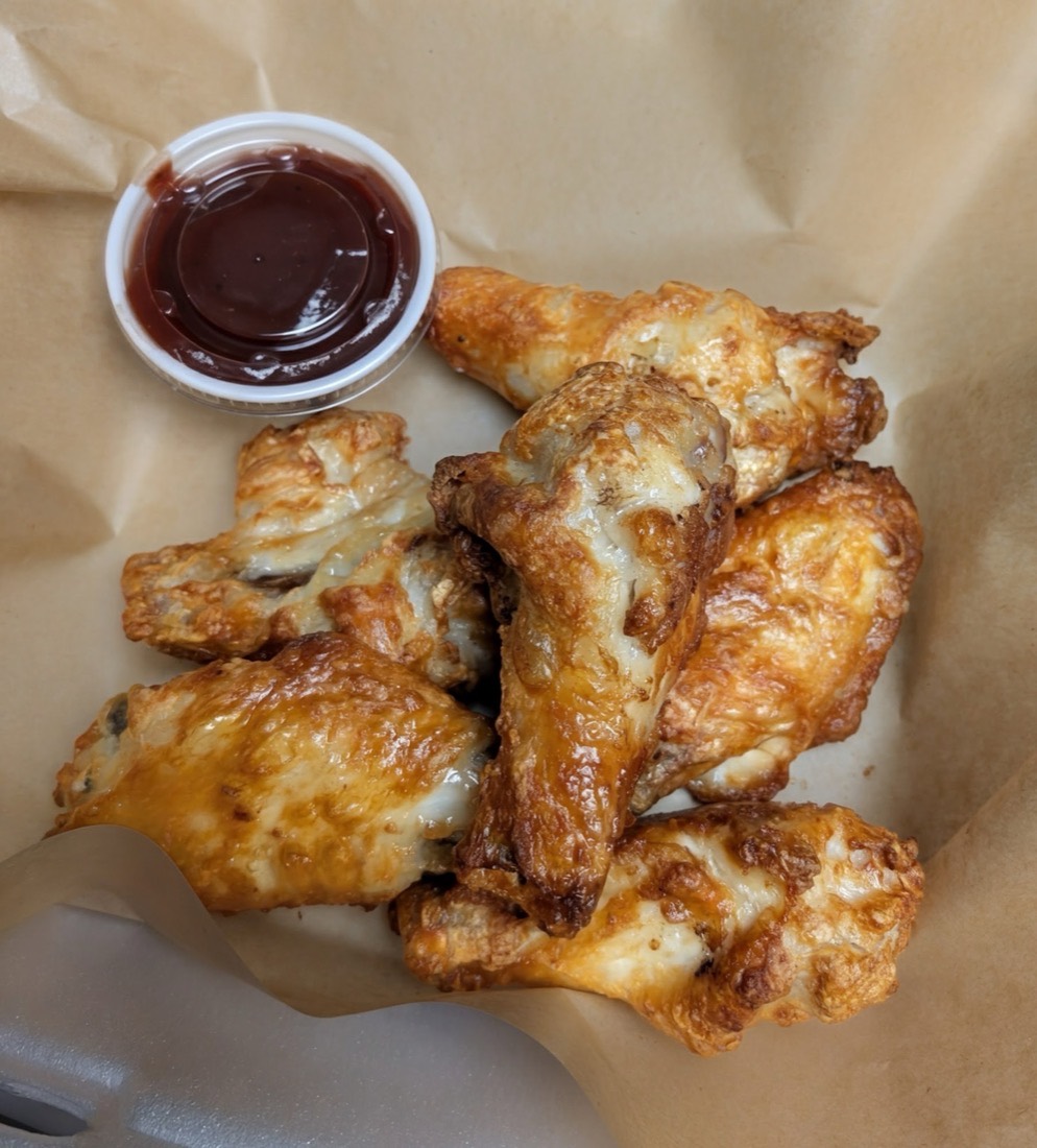 A basket of golden pork wings with a side of barbecue sauce